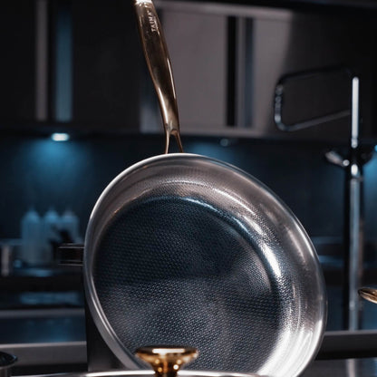 A close up of a Titanium steel frying pan with a textured non-stick interior and a metallic gold handle, shown in a dark modern kitchen setting.