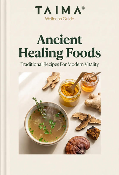 Front cover of a wellness guide titled "Ancient Healing Foods" by TAIMA, with the subtitle "Traditional Recipes For Modern Vitality." The cover shows a bowl of soup surrounded by herbs, mushrooms, honey, and spices on a light cream background.
